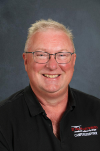 A smiling man with glasses and short hair, wearing a black polo shirt with "St. Vrain Valley Schools" logo.